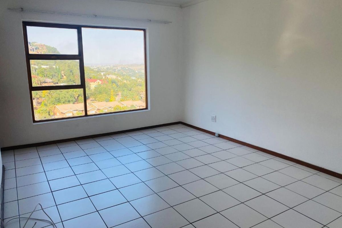 A bright, empty bedroom featuring tiled flooring, a large window with scenic views, and neutral wall finishes.