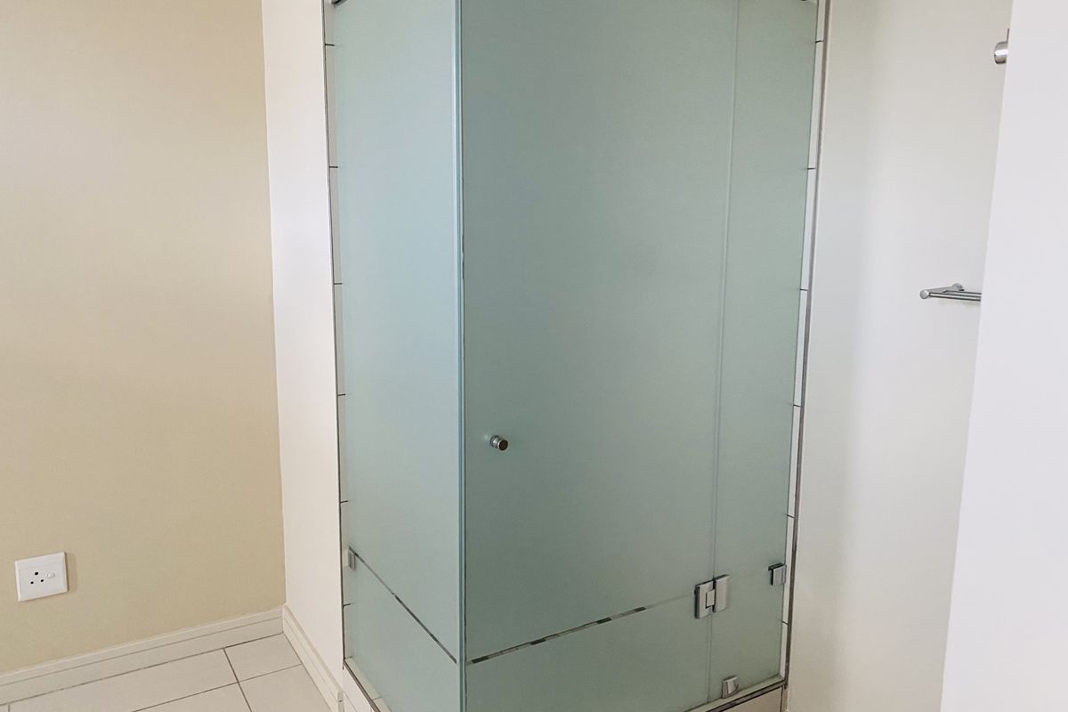 A modern bathroom featuring a glass-enclosed shower cubicle with frosted panels and tiled flooring.