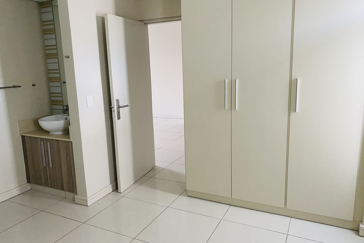 A bedroom featuring built-in wardrobes, tiled flooring, and an integrated vanity area with a basin, leading into an adjacent room.