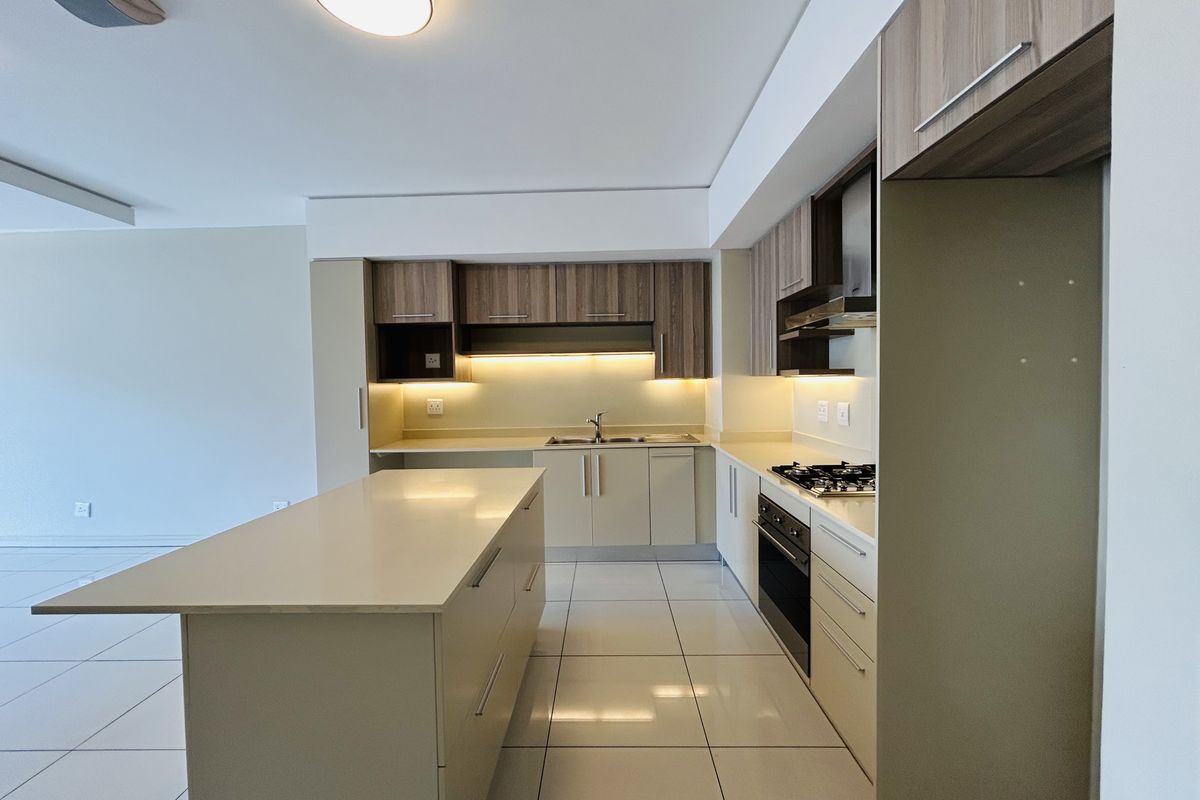 Modern kitchen featuring a central island, quartz countertops, built-in oven, gas hob, and sleek cabinetry with integrated under-cabinet lighting.