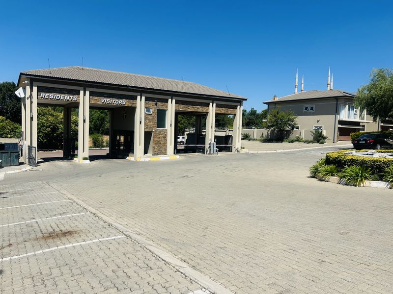 A well-maintained residential security gatehouse featuring stone cladding, tiled roofing, and dedicated lanes for residents and visitors.