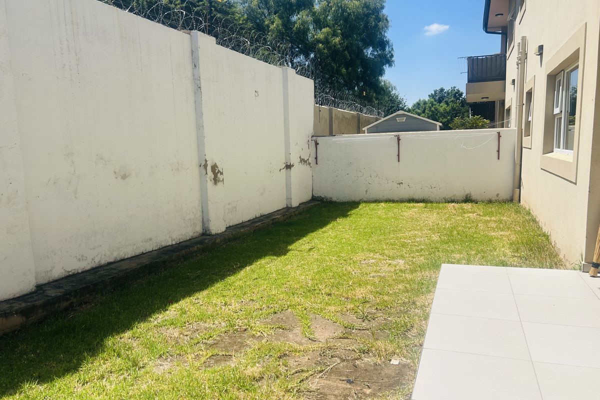 Rear exterior area featuring a tiled patio, a small lawn, and a perimeter wall topped with security razor wire.