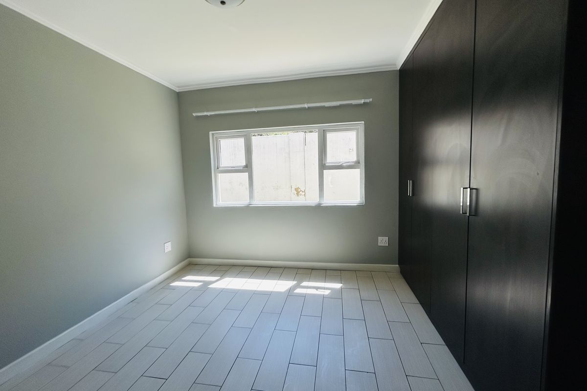 A bright, empty bedroom featuring modern light-colored tiled flooring and dark built-in cupboards, providing a clean and neutral space.