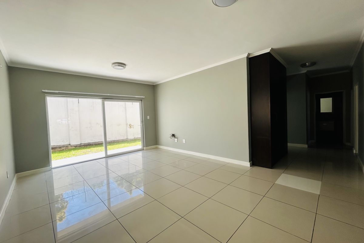A bright, empty living room featuring large format floor tiles, a sliding glass door leading to the exterior, and a built-in storage cupboard.