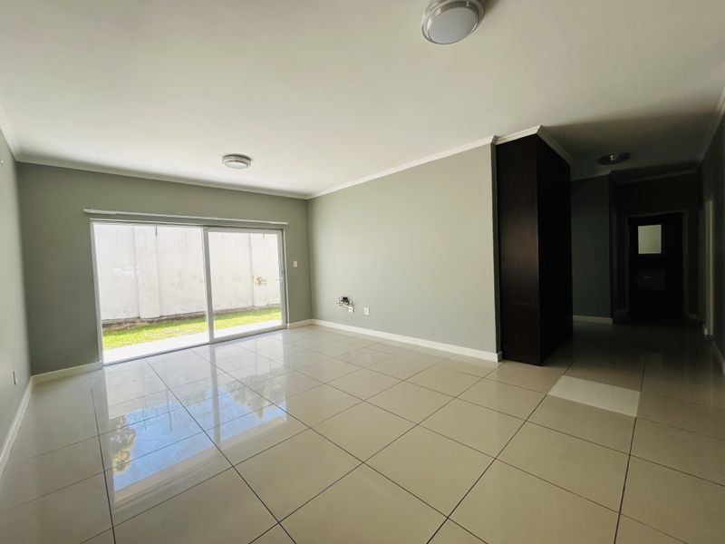 A bright, empty living room featuring large format floor tiles, a sliding glass door leading to the exterior, and a built-in storage cupboard.