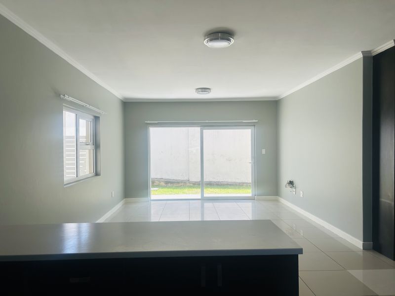 A bright, empty open-plan living area featuring tiled floors, neutral walls, and a sliding glass door leading to the exterior.
