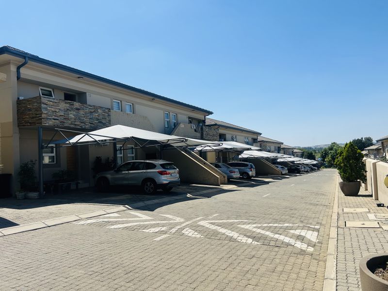 Exterior view of an apartment complex featuring paved driveway, covered parking bays, and modern building facade with stone cladding accents.