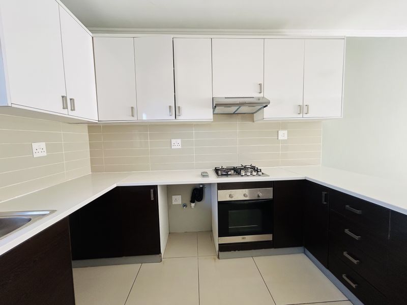 A clean, modern kitchen featuring white upper cabinets, dark lower cabinetry, stone countertops, a gas hob, and a built-in oven.