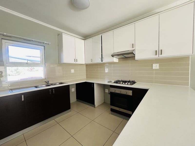 A clean, modern kitchen featuring white upper cabinets, dark lower cabinetry, a gas hob, built-in oven, and neutral tiled splashback.