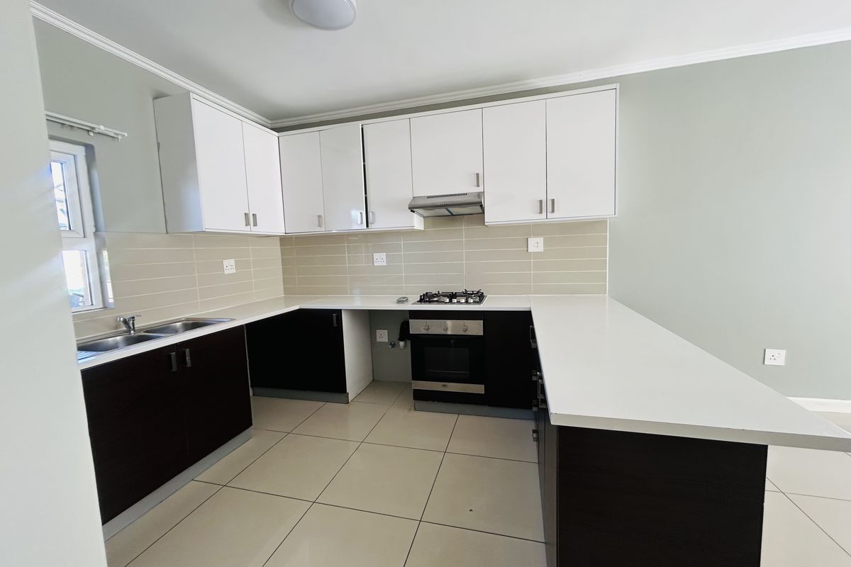 Modern kitchen featuring white upper cabinets, dark lower cabinetry, quartz countertops, built-in gas hob, electric oven, and neutral tiled flooring.