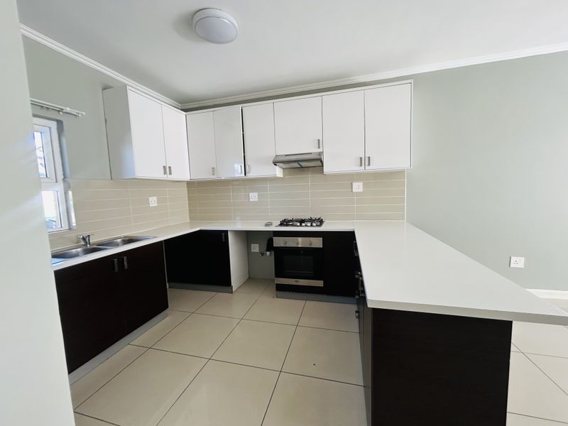 Modern kitchen featuring white upper cabinets, dark lower cabinetry, quartz countertops, built-in gas hob, electric oven, and neutral tiled flooring.