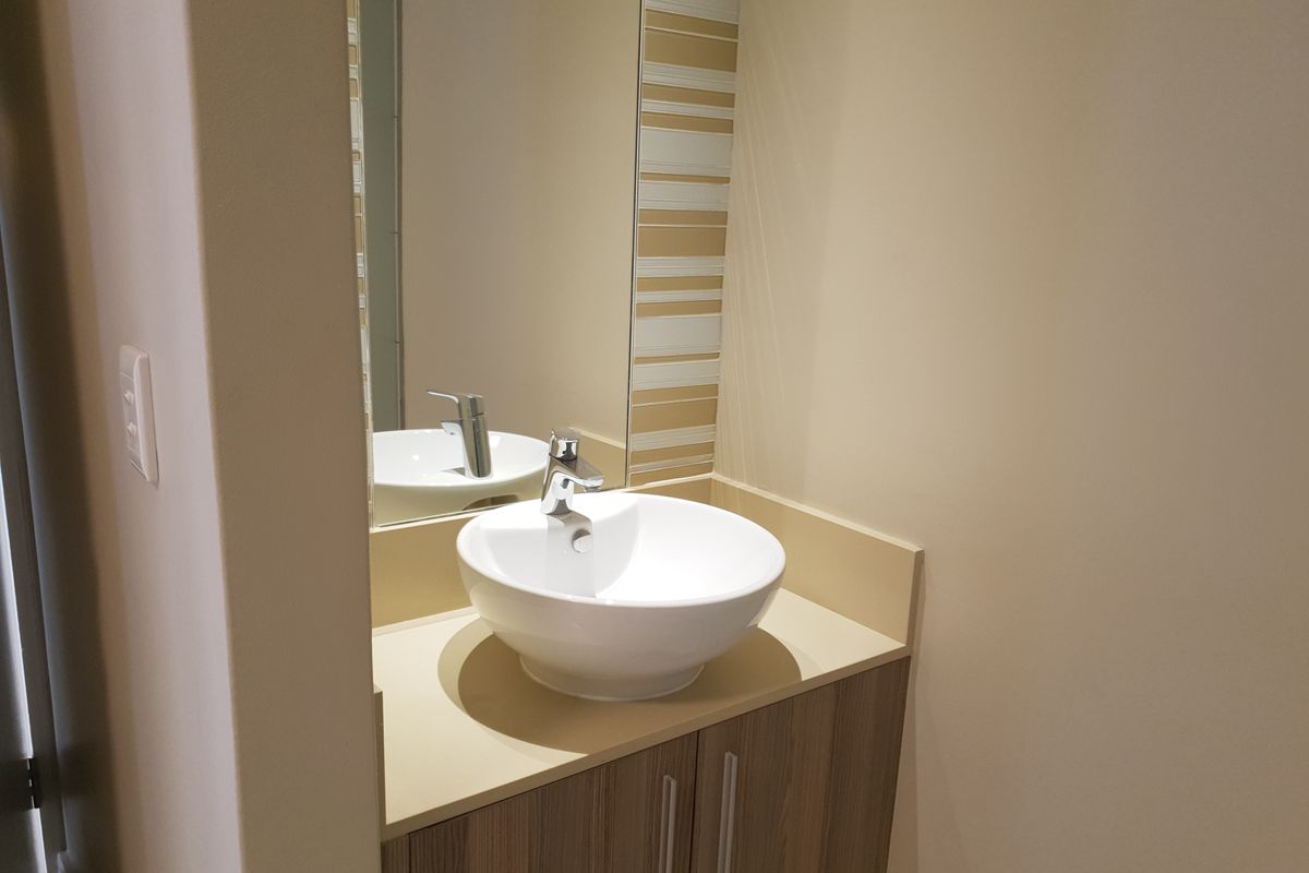 A clean and modern bathroom vanity featuring a white vessel sink, chrome mixer tap, and wood-finish cabinetry with a wall-mounted mirror.