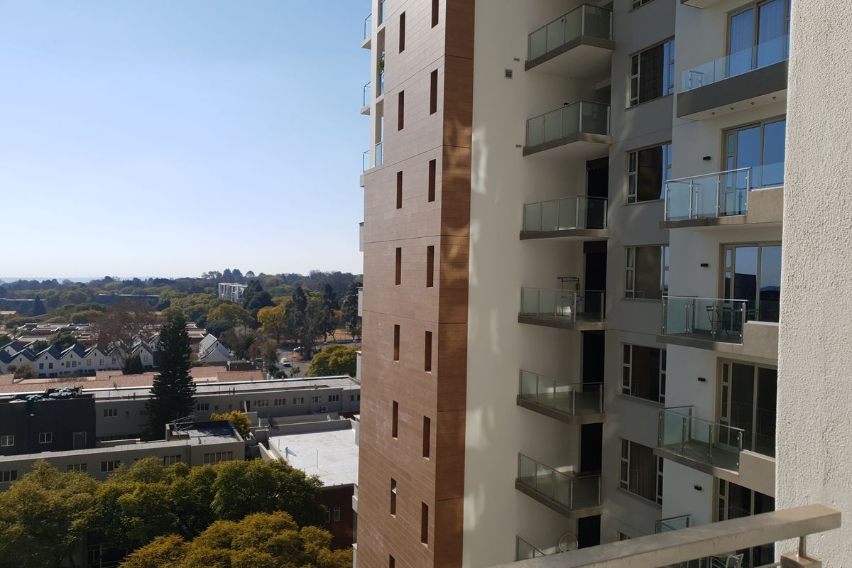 An elevated view of a modern apartment building facade featuring glass-railed balconies and a combination of white and wood-look tiled exterior finishes.