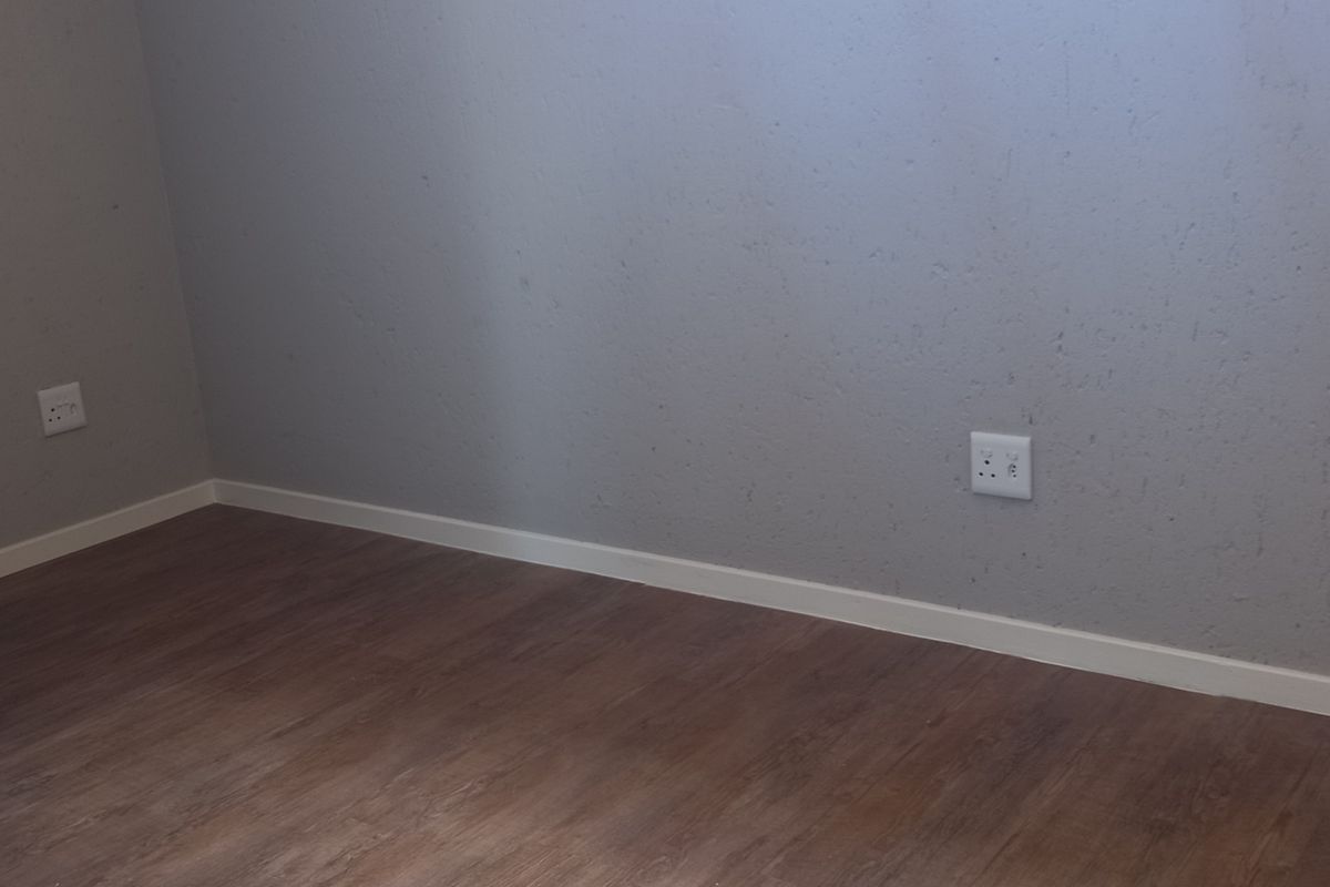 An empty bedroom featuring modern laminate flooring, textured grey walls, and a window, providing a clean and neutral space ready for furnishing.
