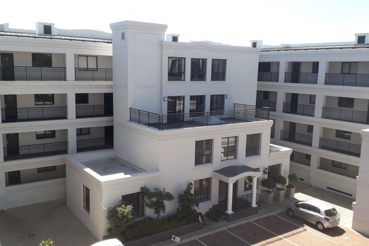 An elevated view of a modern apartment complex featuring white facades, black metal railings, and paved parking areas.