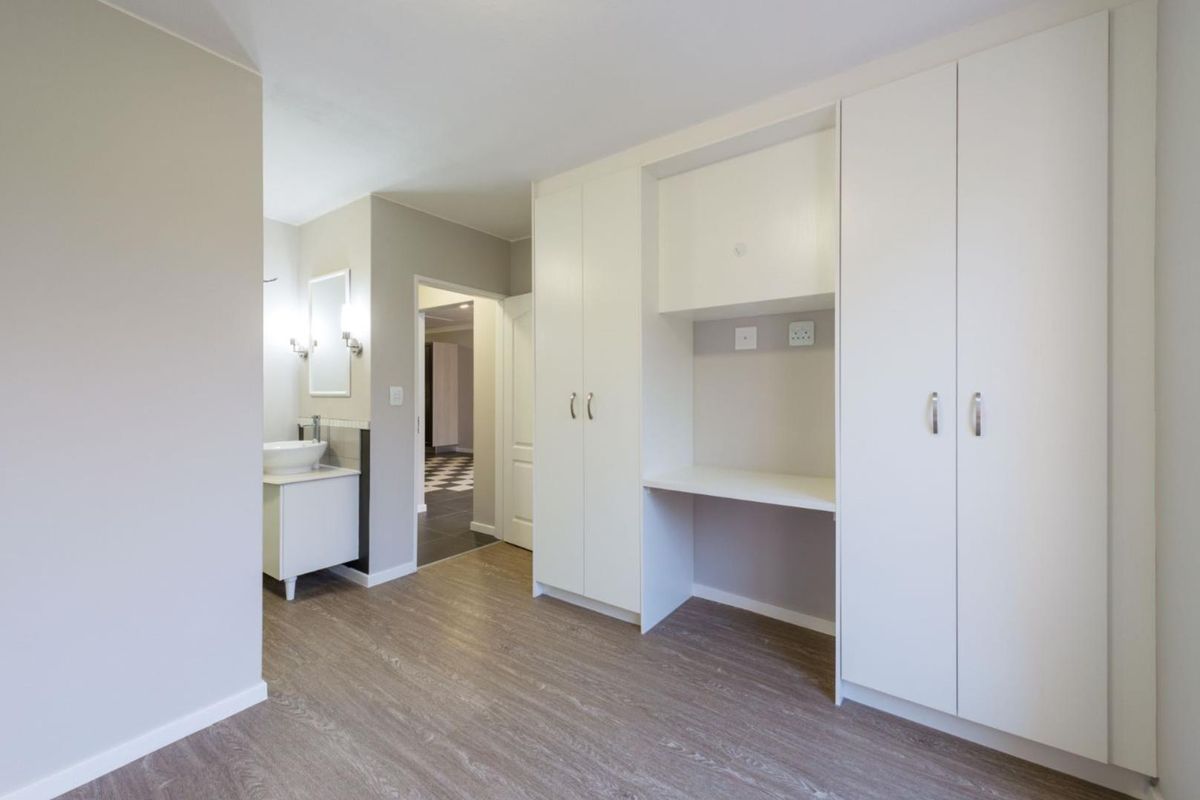 A well-maintained bedroom featuring built-in cupboards, a dedicated desk area, and an en-suite bathroom with a modern vanity.