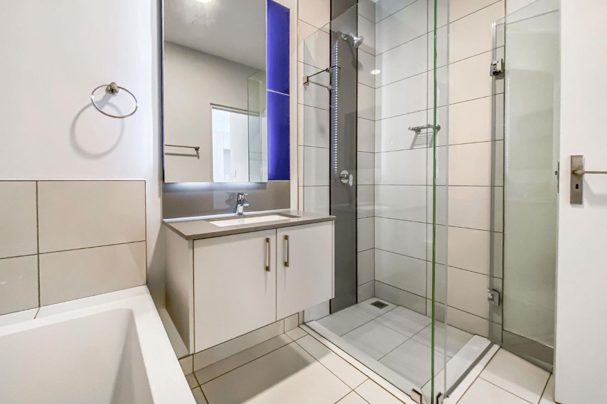 Modern bathroom featuring a floating vanity, glass-enclosed shower, and a separate bathtub with neutral tiled finishes.