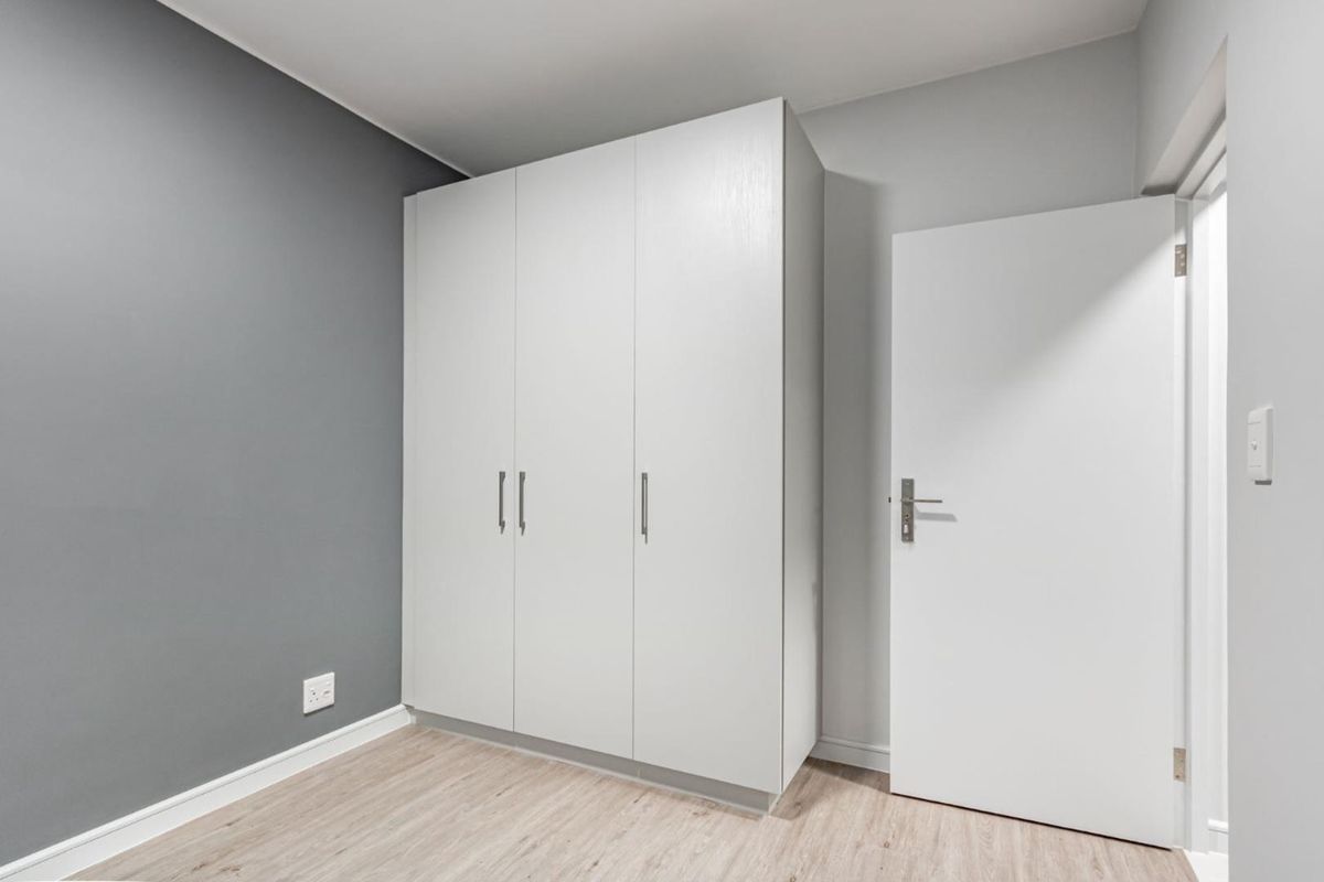 A clean, modern bedroom featuring light wood-look laminate flooring, a large white built-in wardrobe, and a contrasting grey accent wall.