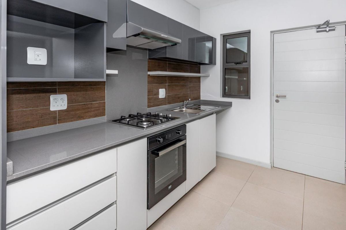 Modern kitchen featuring sleek grey and white cabinetry, stone countertops, built-in gas hob, oven, extractor fan, and tiled finishes.