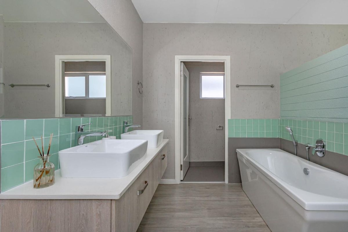 Modern bathroom featuring a double vanity with vessel sinks, a large wall mirror, and a built-in bathtub with green tiled splashbacks.