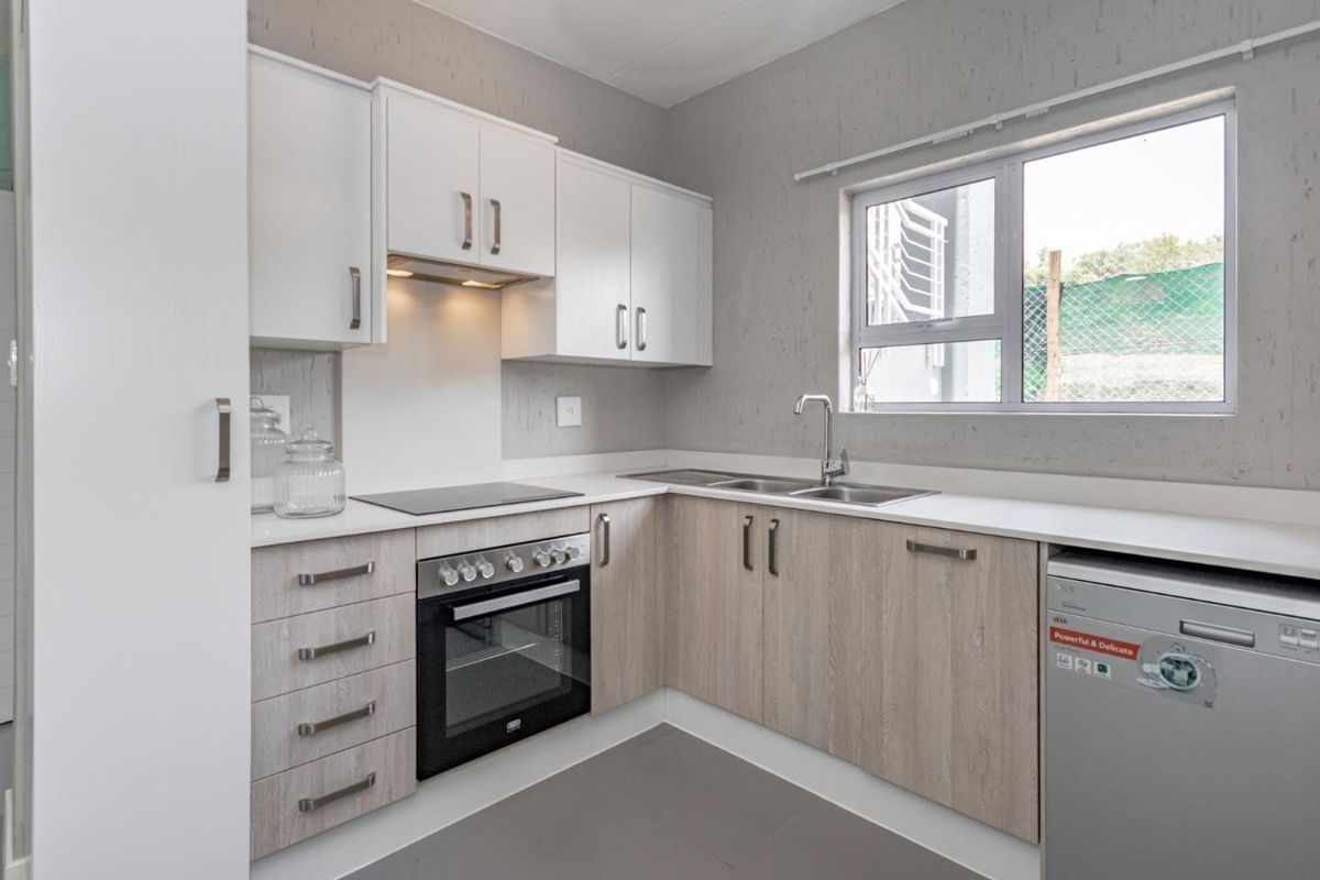 Modern kitchen featuring light wood-look cabinetry, white upper cabinets, integrated electric hob and oven, and a stainless steel sink with a window view.