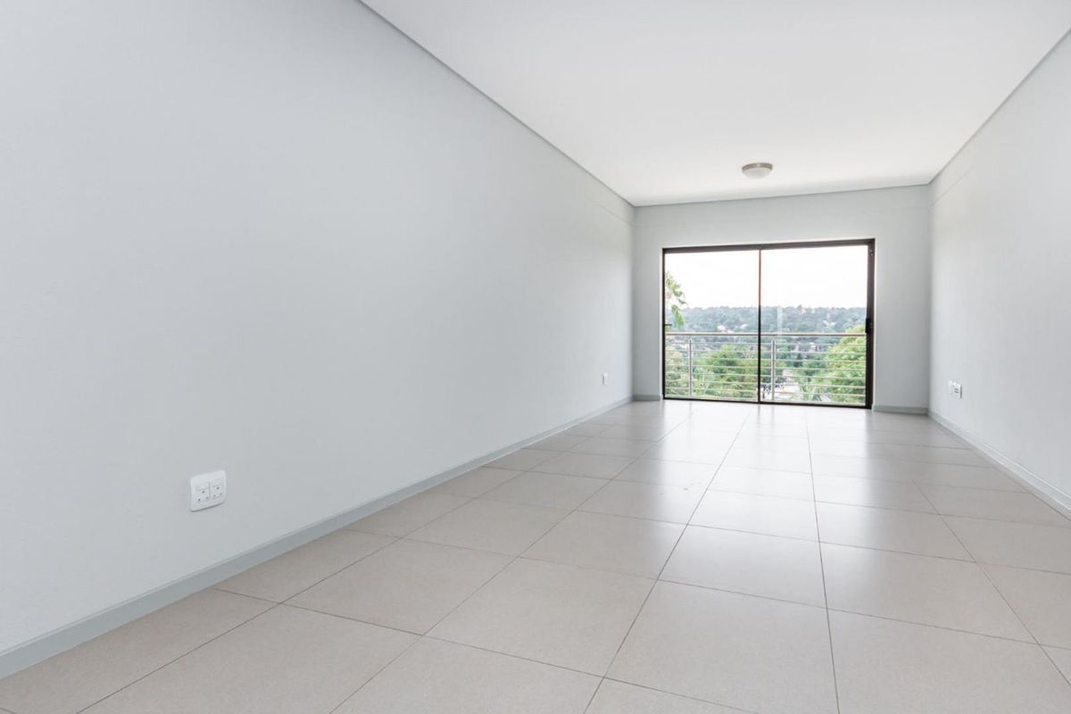 A bright, empty living room featuring neutral tiled flooring and a large sliding glass door that opens to a balcony with scenic views.