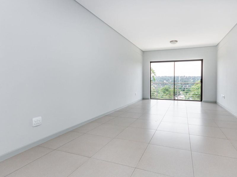 A bright, empty living room featuring neutral tiled flooring and a large sliding glass door that opens to a balcony with scenic views.