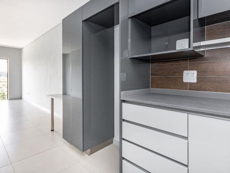 Modern kitchen area featuring sleek grey and white cabinetry, stone countertops, and tiled backsplash, leading to an open living space with balcony access.