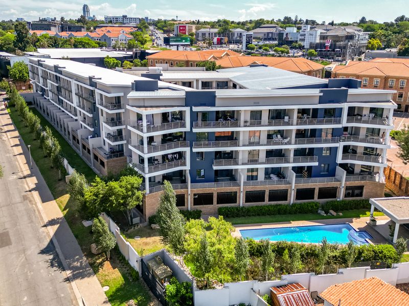 Aerial view of a modern multi-story apartment complex featuring private balconies, a swimming pool, and landscaped grounds in a suburban setting.