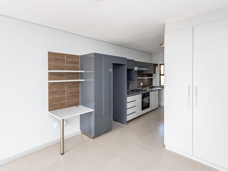 Modern kitchen featuring sleek grey and white cabinetry, built-in oven and hob, tiled backsplash, and an integrated workspace area.