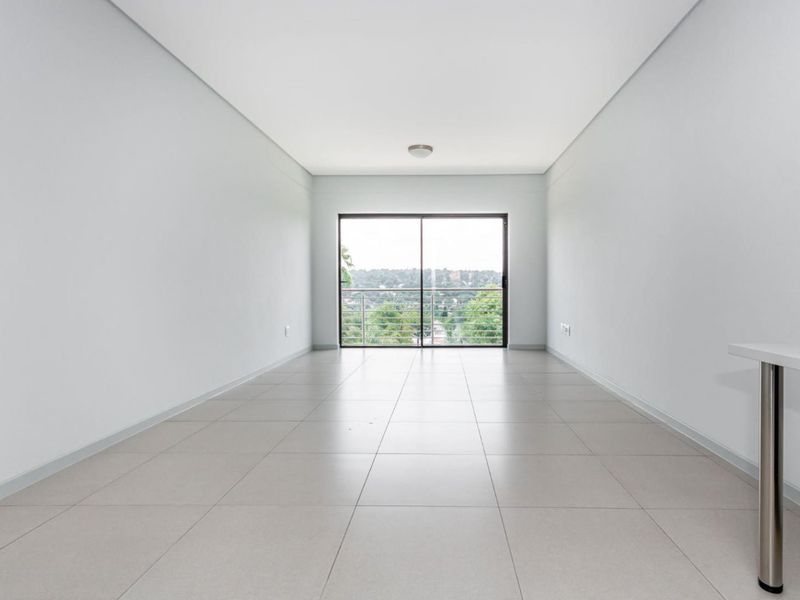 A bright, empty living area featuring neutral tiled flooring and a large sliding glass door that opens to a balcony with scenic views.