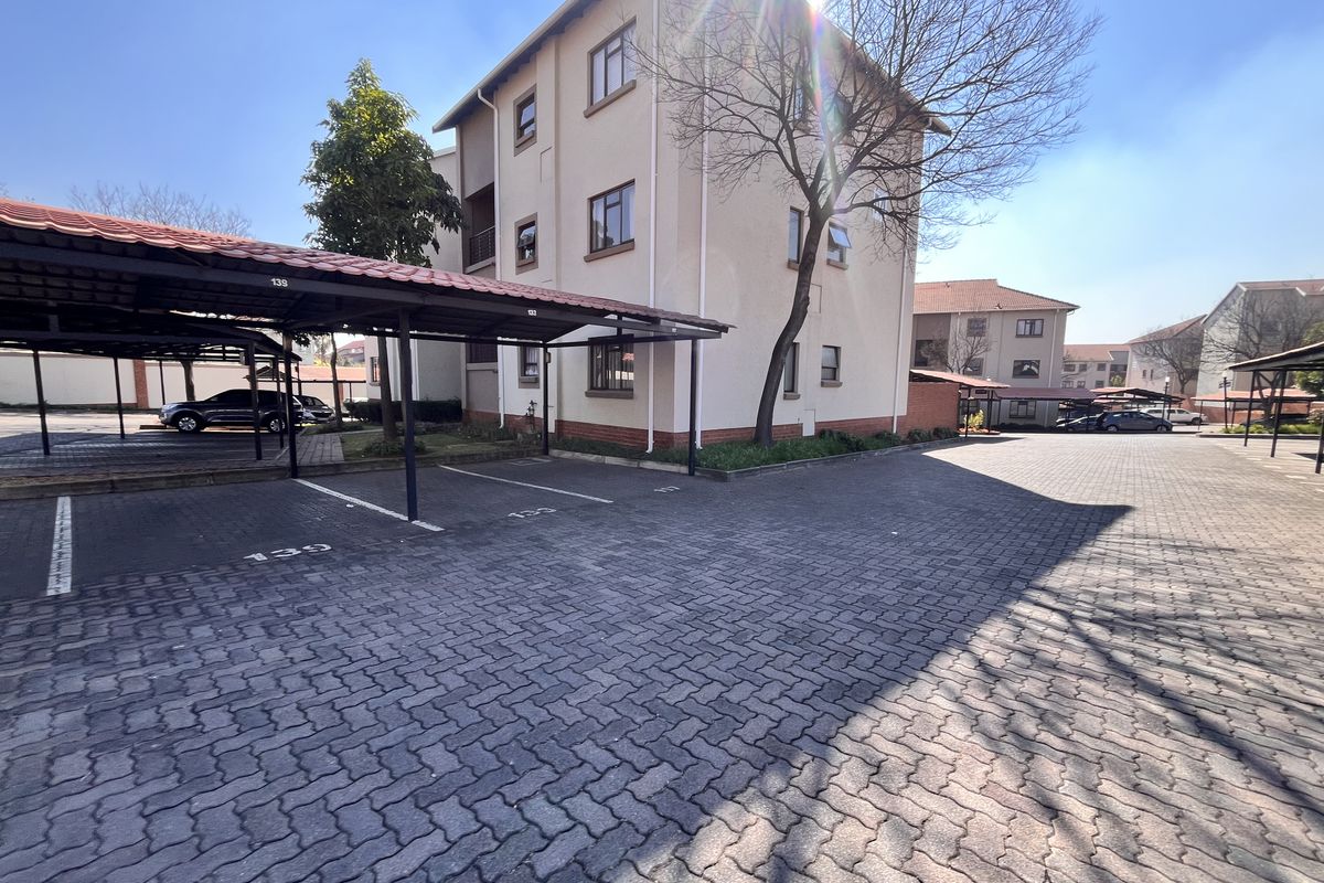 Exterior view of a multi-story apartment complex featuring paved parking areas and covered parking bays.