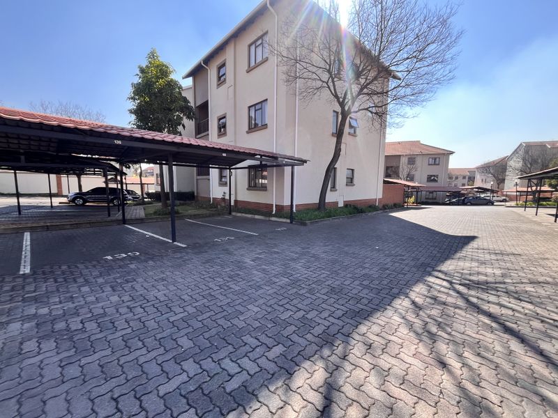 Exterior view of a multi-story apartment complex featuring paved parking areas and covered parking bays.