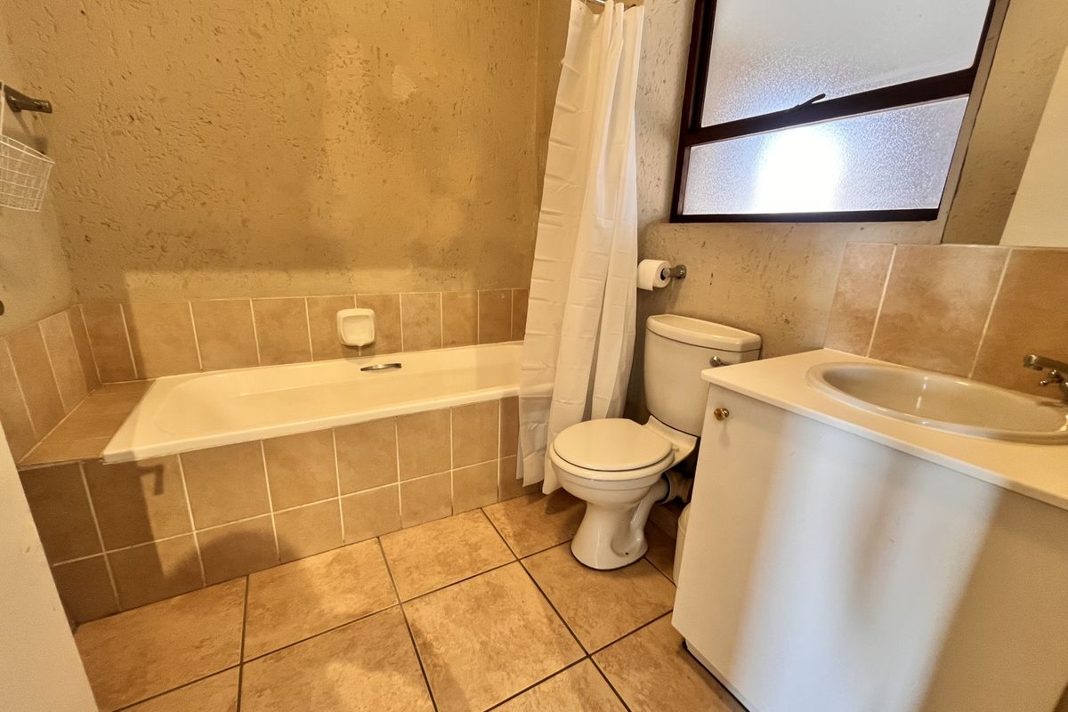 A functional bathroom featuring a bathtub, toilet, and vanity basin with tiled flooring and splashbacks, requiring cosmetic updates to the wall finishes.