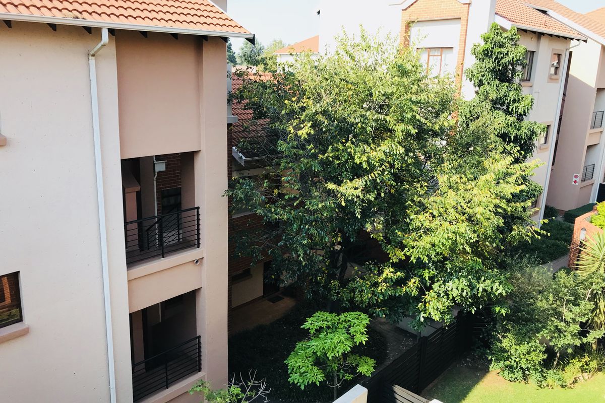 An elevated view of the apartment complex exterior, featuring multi-level balconies, terracotta roofing, and a well-maintained communal garden area.