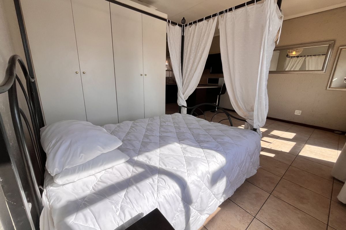 A bedroom featuring built-in cupboards and tiled flooring, with a view into the adjacent kitchen area.