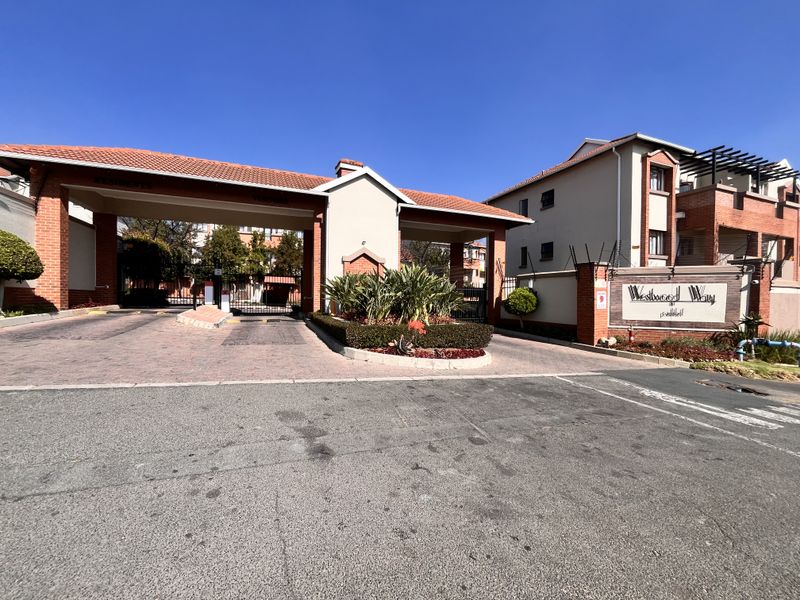 The main entrance and security gatehouse of Westwood Way apartment complex, featuring brick construction, tiled roofing, and paved access.
