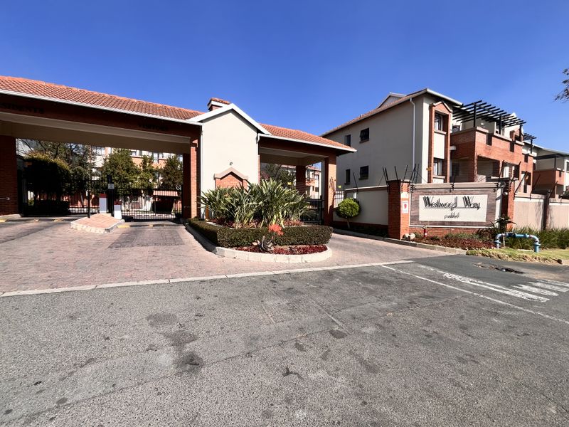 The main entrance to Westwood Way apartment complex, featuring a secure gated access point, brick paving, and well-maintained perimeter walls with electric fencing.