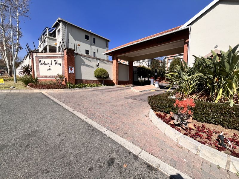 The entrance to Westwood Way apartment complex featuring a secure gated access point, brick paved driveway, and well-maintained perimeter landscaping.