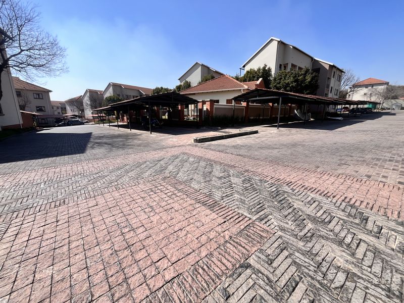 A wide-angle view of the apartment complex parking area featuring paved driveways and multiple covered parking bays.
