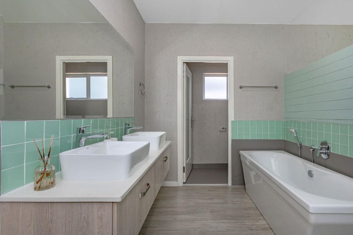 Modern bathroom featuring a double vanity with vessel sinks, a built-in bathtub, and stylish mint green tiled splashbacks.