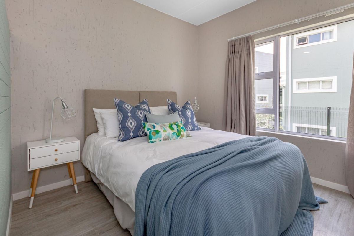 A well-maintained bedroom featuring neutral textured walls, laminate flooring, and a large window with natural light.