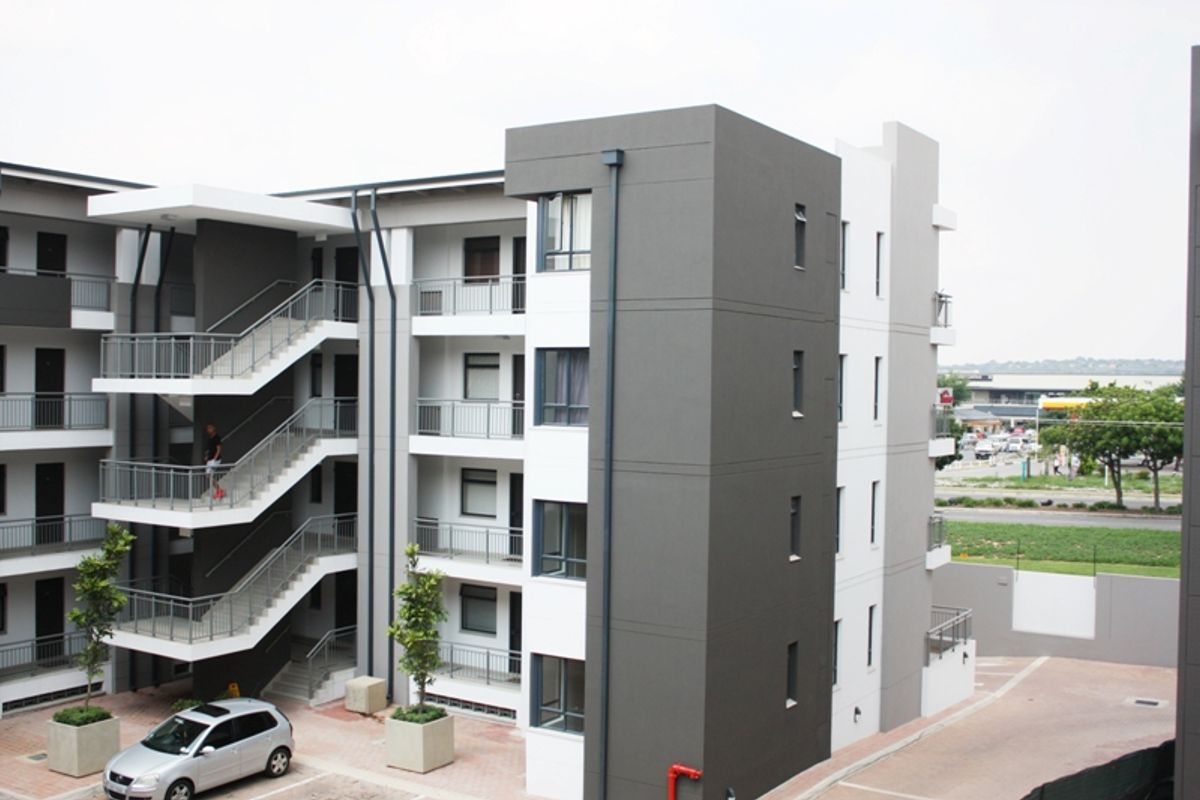 Exterior view of a modern multi-story apartment complex featuring external staircases, metal balustrades, and a paved courtyard area.