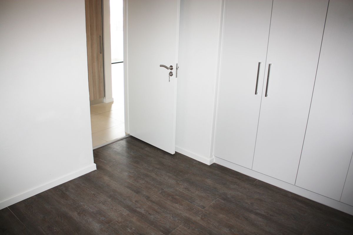 A clean, empty bedroom featuring modern laminate flooring and white built-in wardrobes, offering a neutral canvas for personalization.