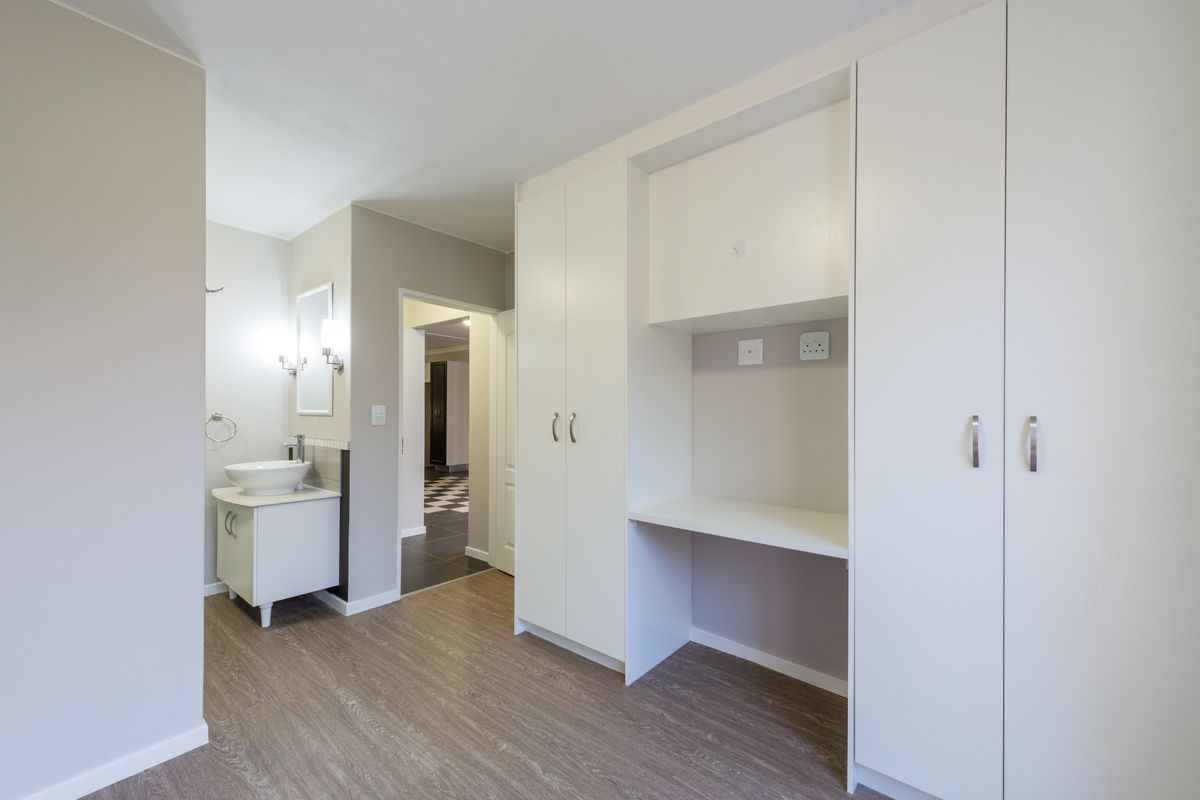 A well-maintained bedroom featuring built-in cupboards, a dedicated desk area, and an en-suite vanity basin with modern finishes.