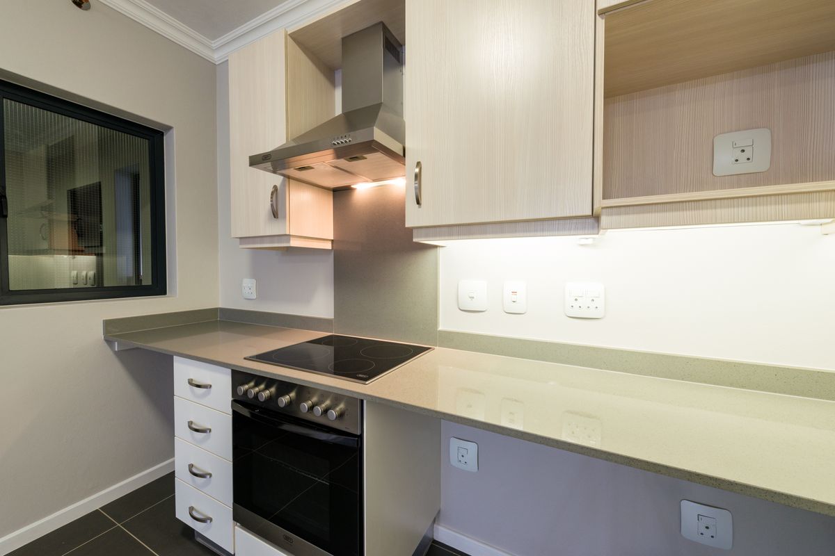 Modern kitchen featuring light wood-grain cabinetry, stone countertops, a built-in electric oven, and a stainless steel extractor fan.