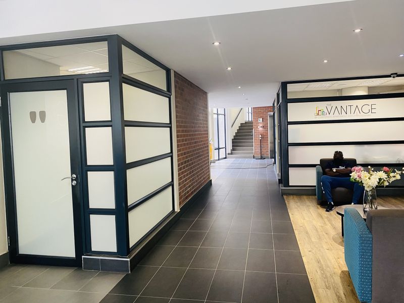 Modern apartment building entrance lobby featuring a combination of tiled and laminate flooring, glass partitions, and an exposed brick accent wall.