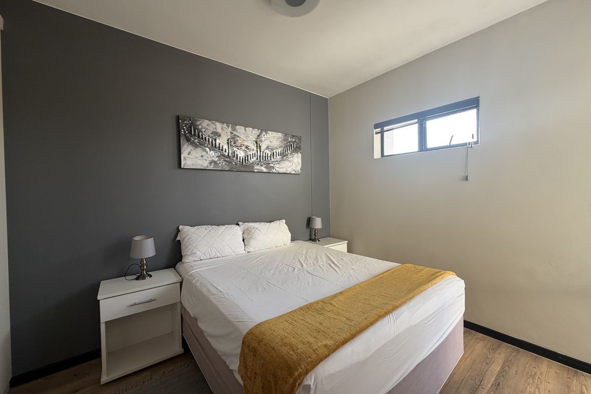 A well-maintained bedroom featuring laminate flooring, a high-level window for natural light, and a neutral color palette with a dark accent wall.
