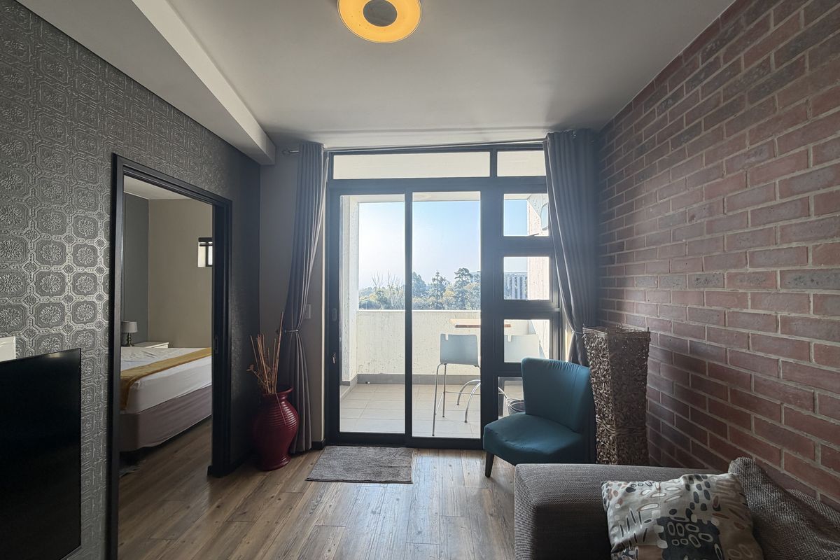 A well-maintained living room featuring an exposed brick wall, textured wallpaper, and large sliding glass doors leading to a private balcony.