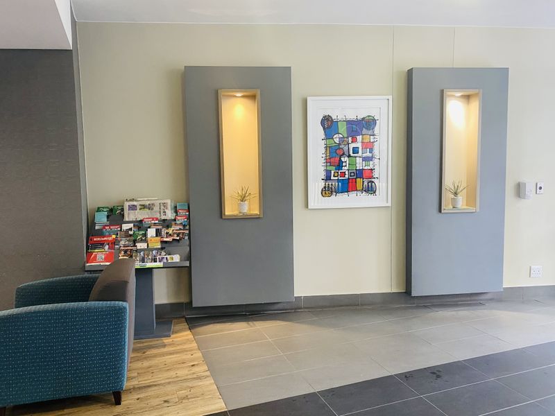 A modern apartment building entrance lobby featuring decorative recessed wall niches with integrated accent lighting and neutral tiled flooring.